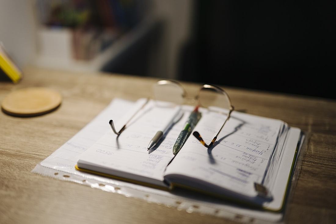 Schreibtisch mit Notizbuch, Stiften und Brille